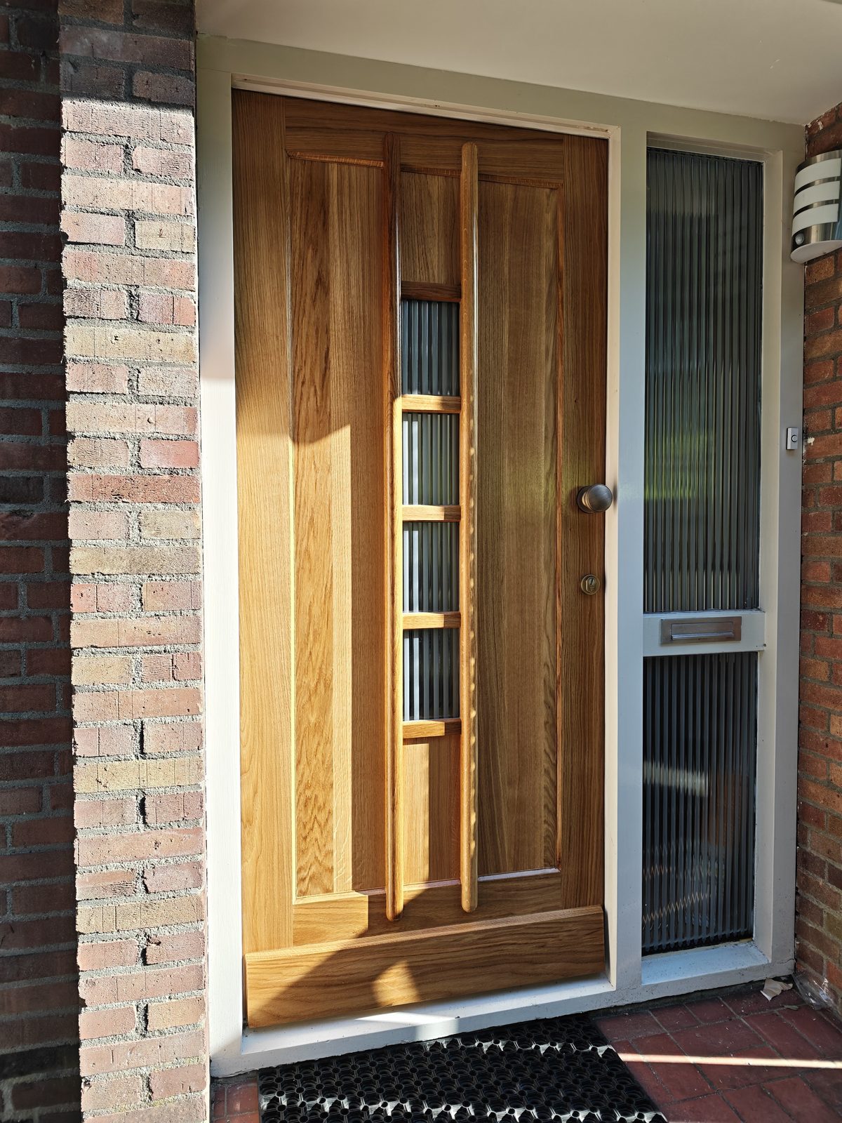 Houten voordeur op maat in eiken met glasstroken, in een bakstenen gevel