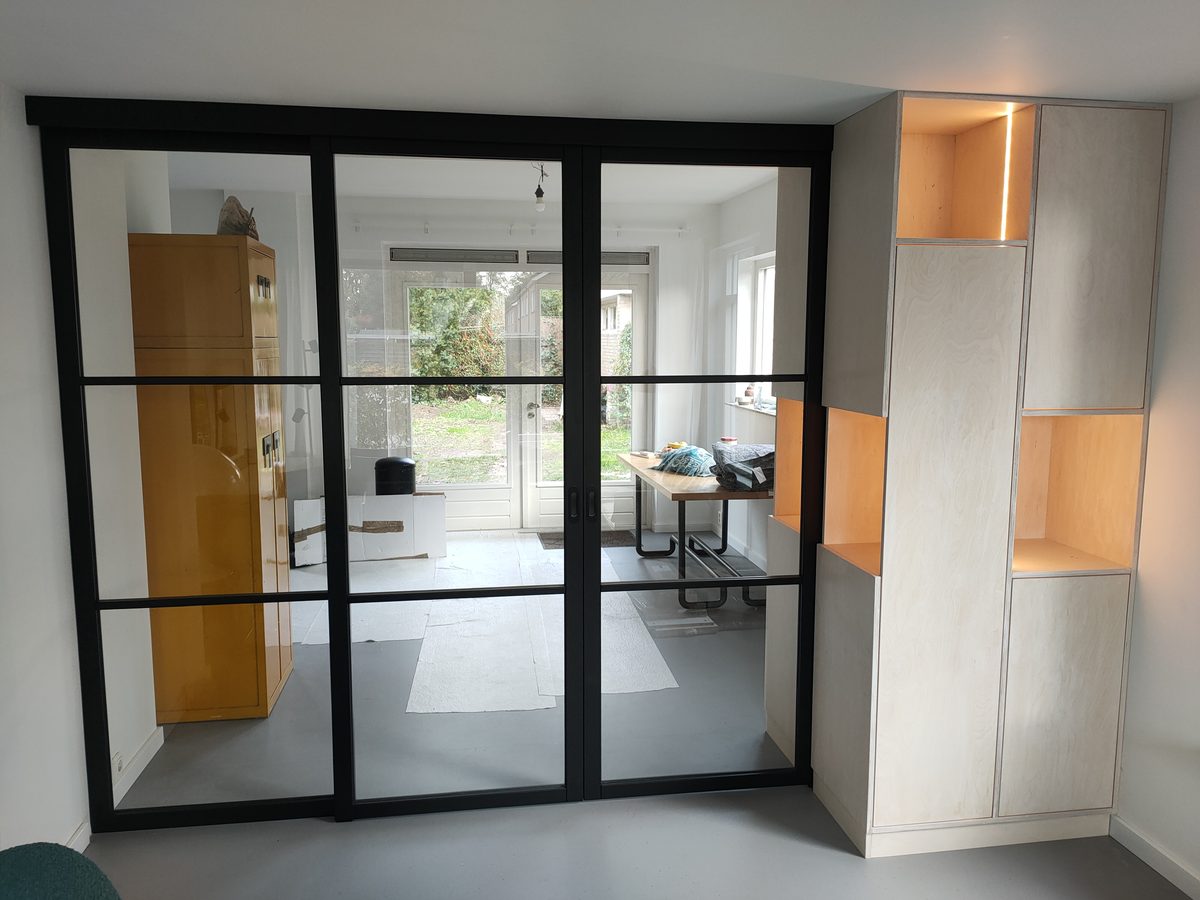 Dubbele glazen schuifdeur met zwart kader en kasten op maat in een woonkamer