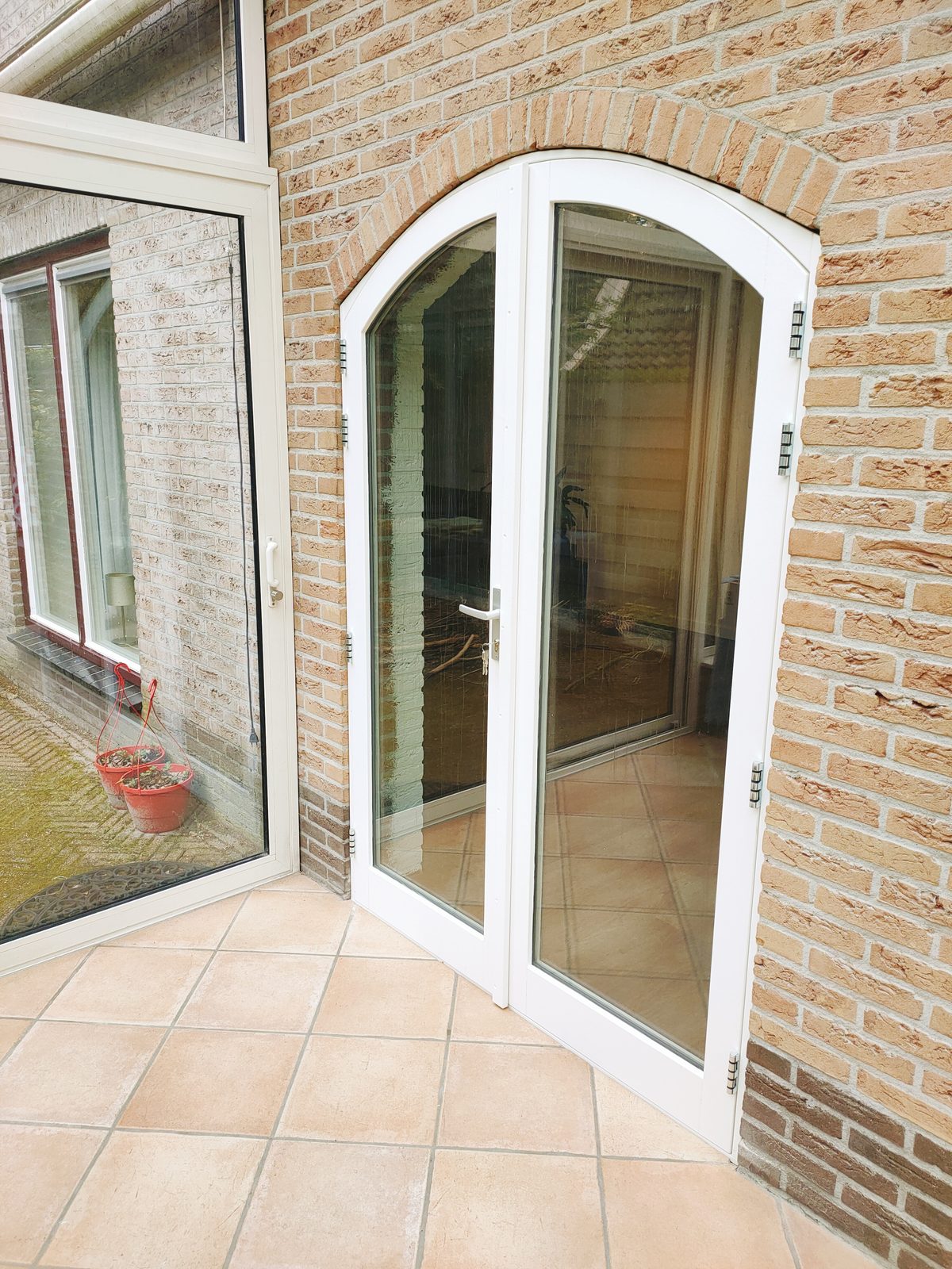 Witte openslaande tuindeuren op maat met boogvorm in een bakstenen gevel