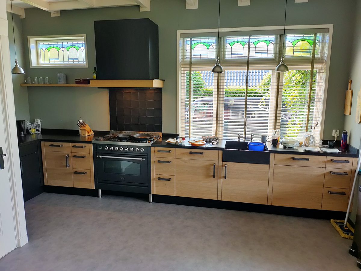 Eikenhouten keuken op maat met zwart aanrechtblad, fornuis en afzuigkap, in een woning met glas-in-lood