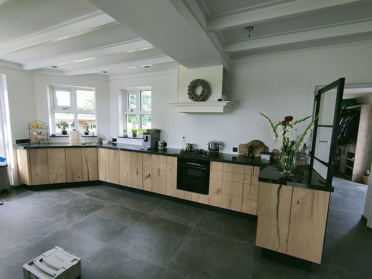 Lichte houten keuken in L-vorm met zwart werkblad en schouw, op maat gemaakt
